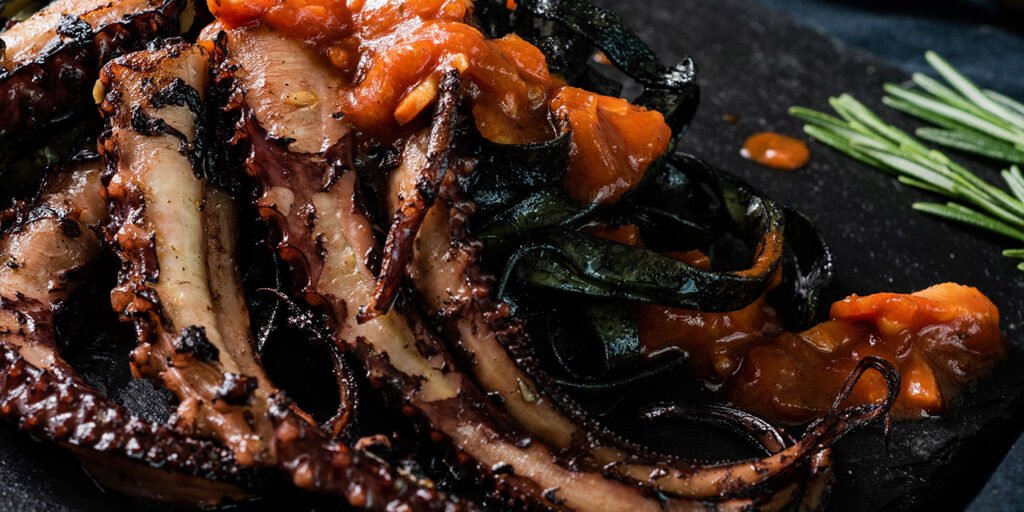 Pulpo a la plancha sobre pasta negra y tomate frito con ajo